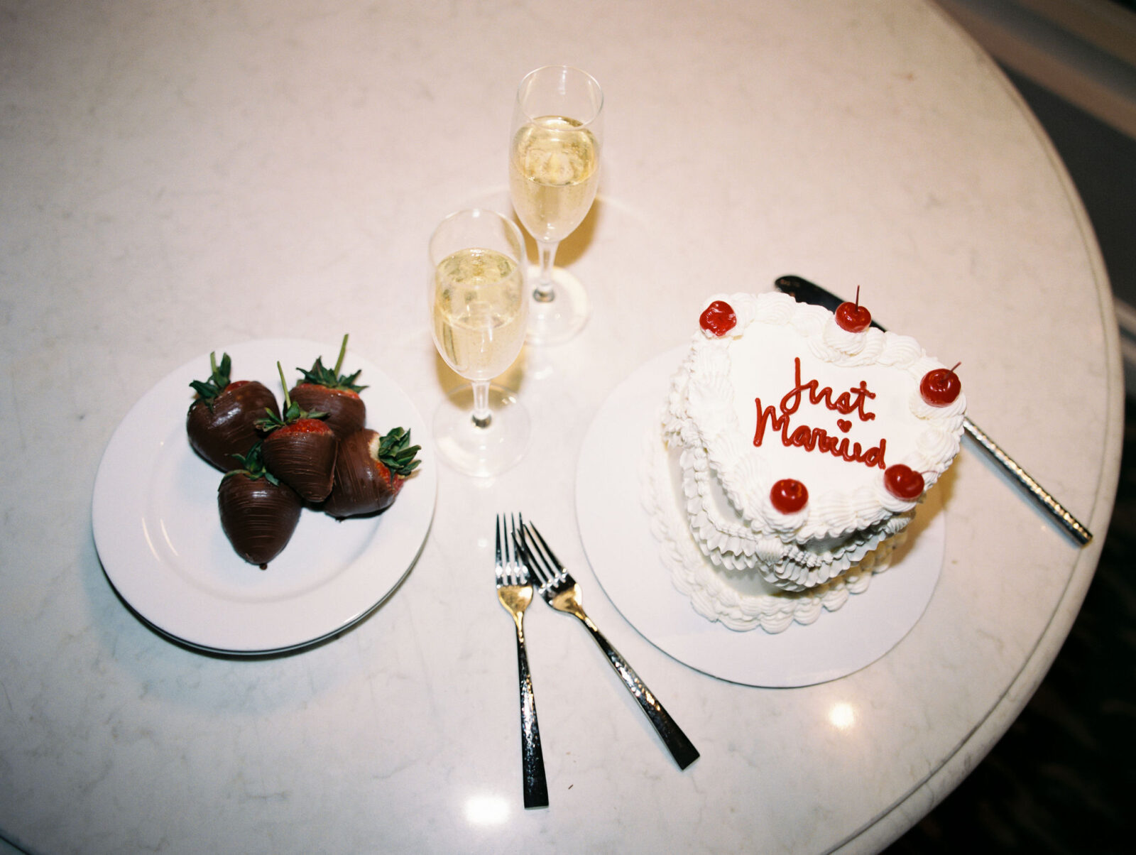 Flatlay shot of chocolate covered strawberries and a small heart-shaped elopement cake that says "just married"