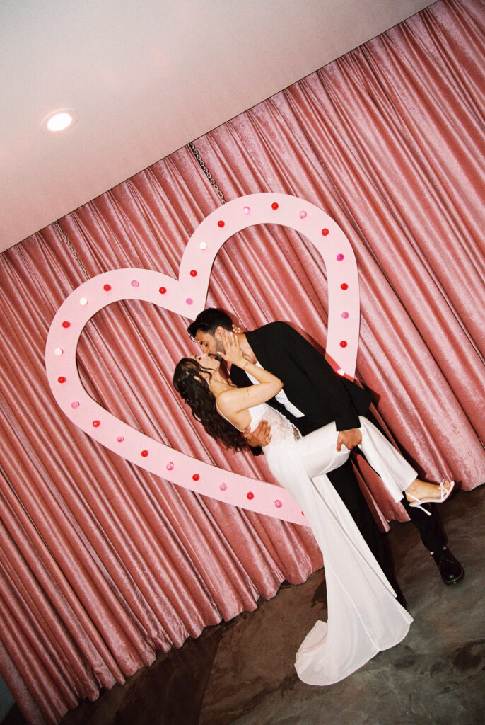 Couple kissing in front of the pink neon heart at Sure Thing Chapel
