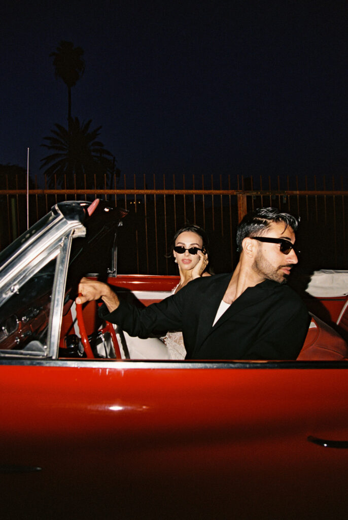 Bride and groom wearing sunglasses for their Las Vegas elopement shoot in a red convertible