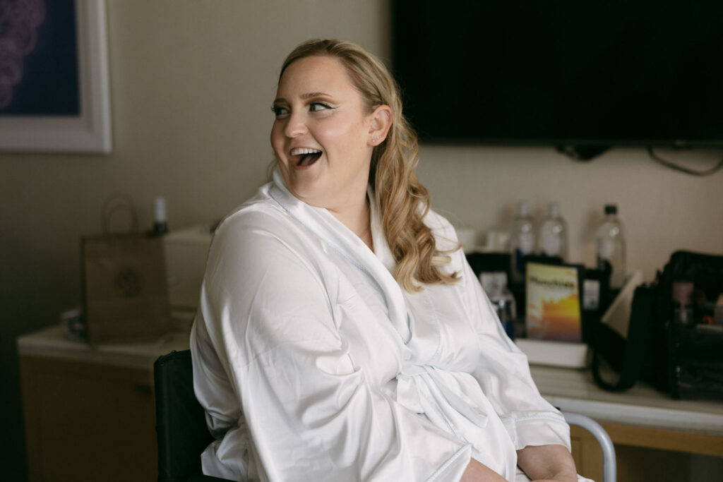 Bride smiling at her bridesmaids as she gets her makeup done