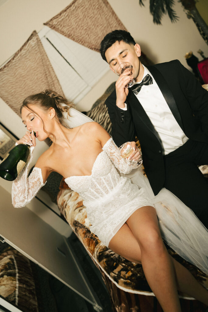 Bride and groom drinking champagne side by side on a zebra-print bed during their fun retro Las Vegas elopement.