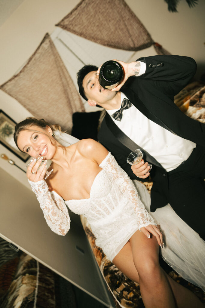 Bride and groom drinking champagne side by side on a zebra-print bed during their fun retro Las Vegas elopement.