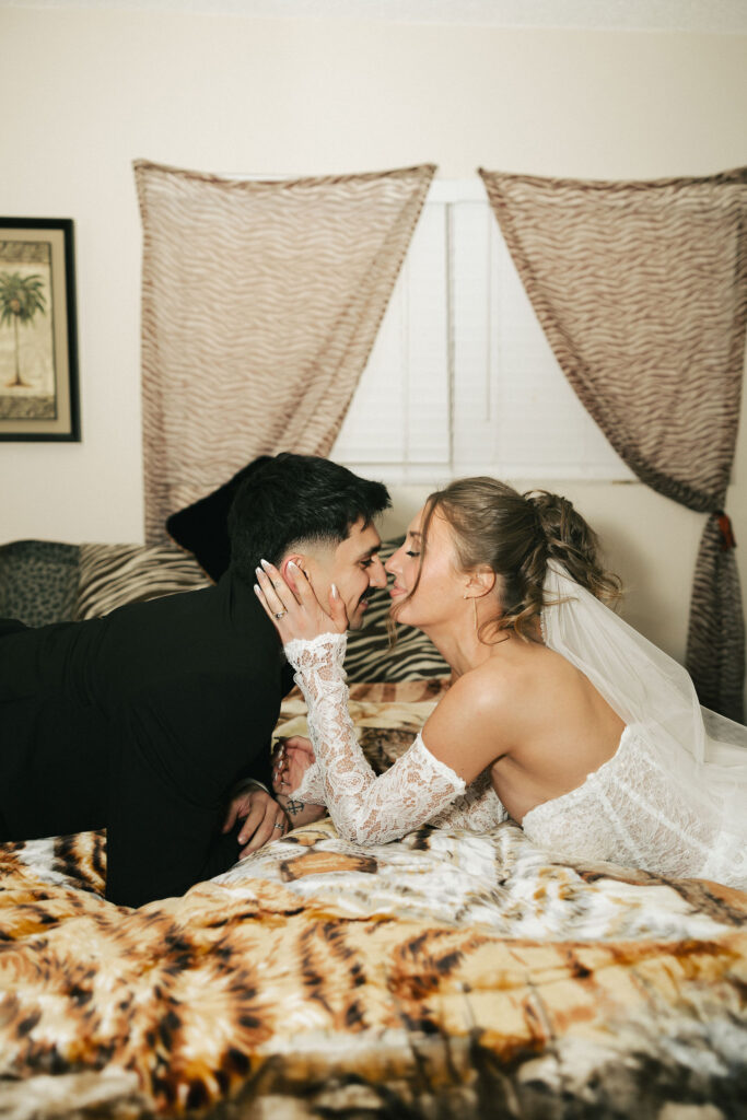 Bride and groom sharing a romantic moment lying on a bold animal print bedspread at their retro Las Vegas elopement.