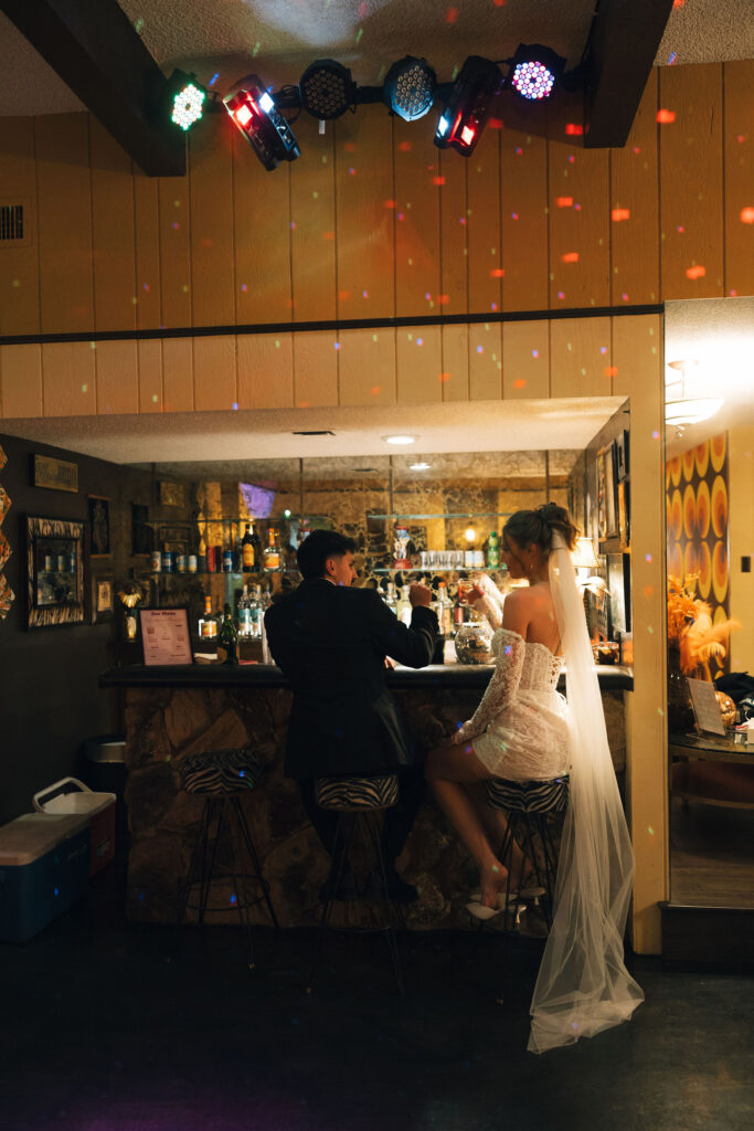 Bride and groom clinking glasses together at a vintage bar with disco lights shining during their retro Las Vegas elopement.