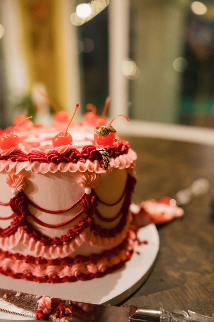 Close-up of a pink and red vintage-inspired wedding cake topped with cherries and wedding rings at a retro Las Vegas elopement reception.