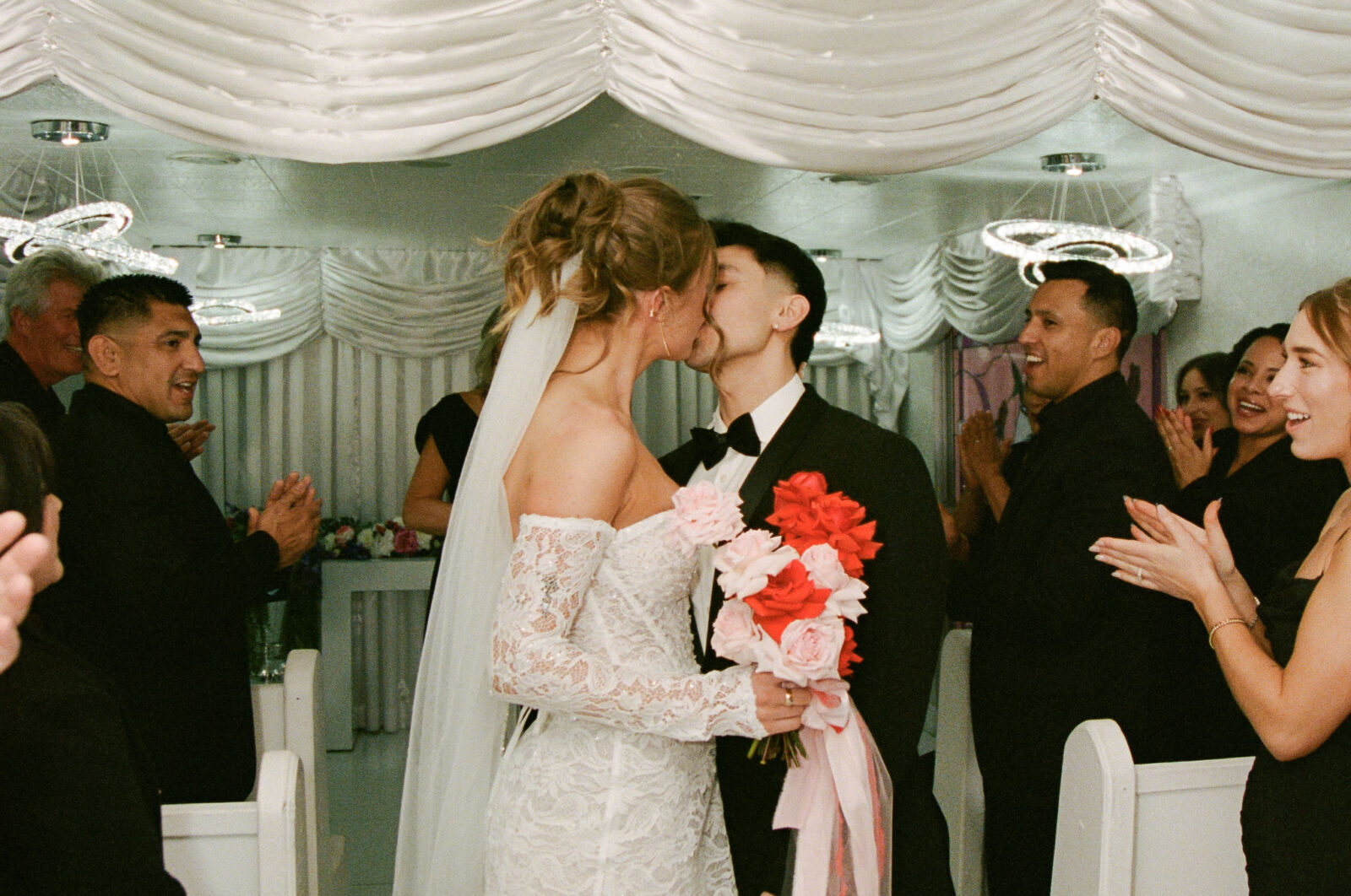 Bride and groom sharing a kiss at the altar inside The Little White Wedding Chapel while guests clap on film