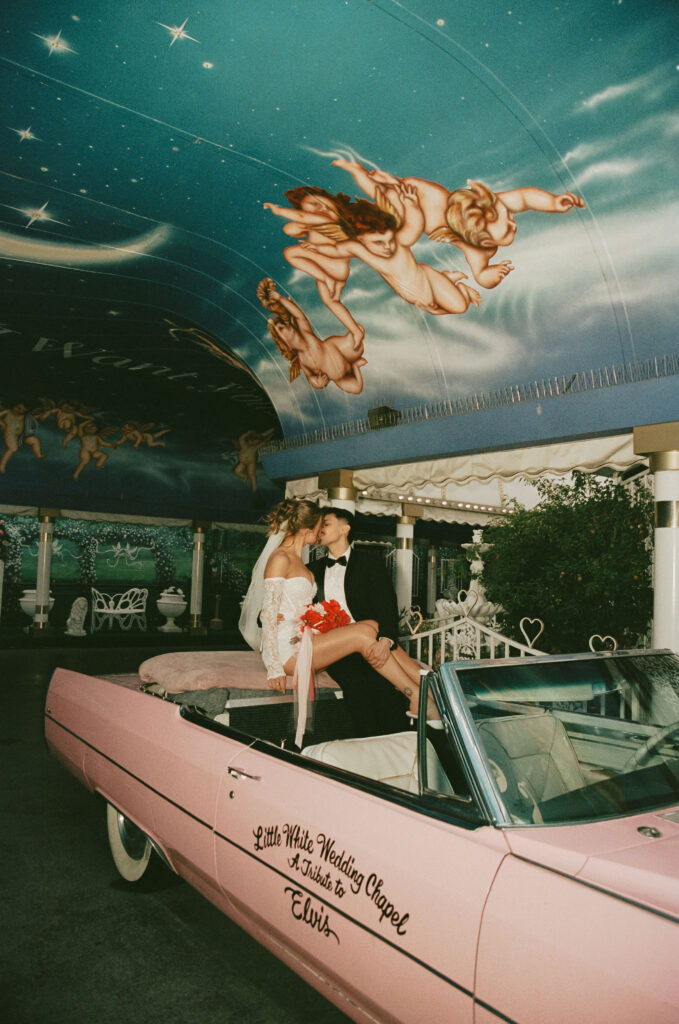 Bride and groom celebrating in the back of the pink Cadillac under the chapel’s starry painted ceiling.