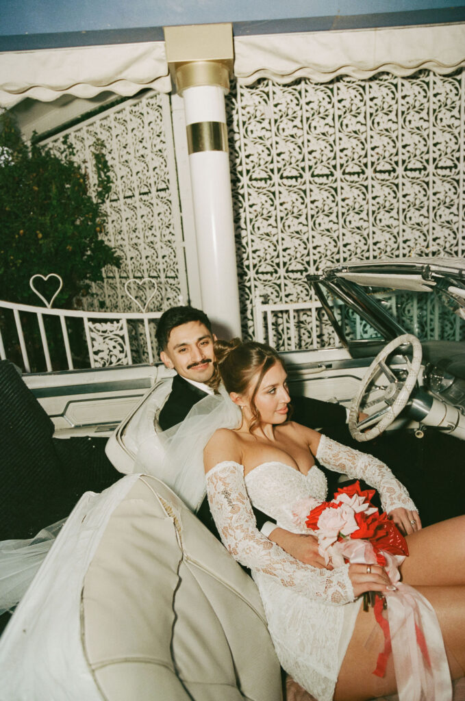Bride leaning against the groom in the front seat of the pink Cadillac at The Little White Wedding Chapel.
