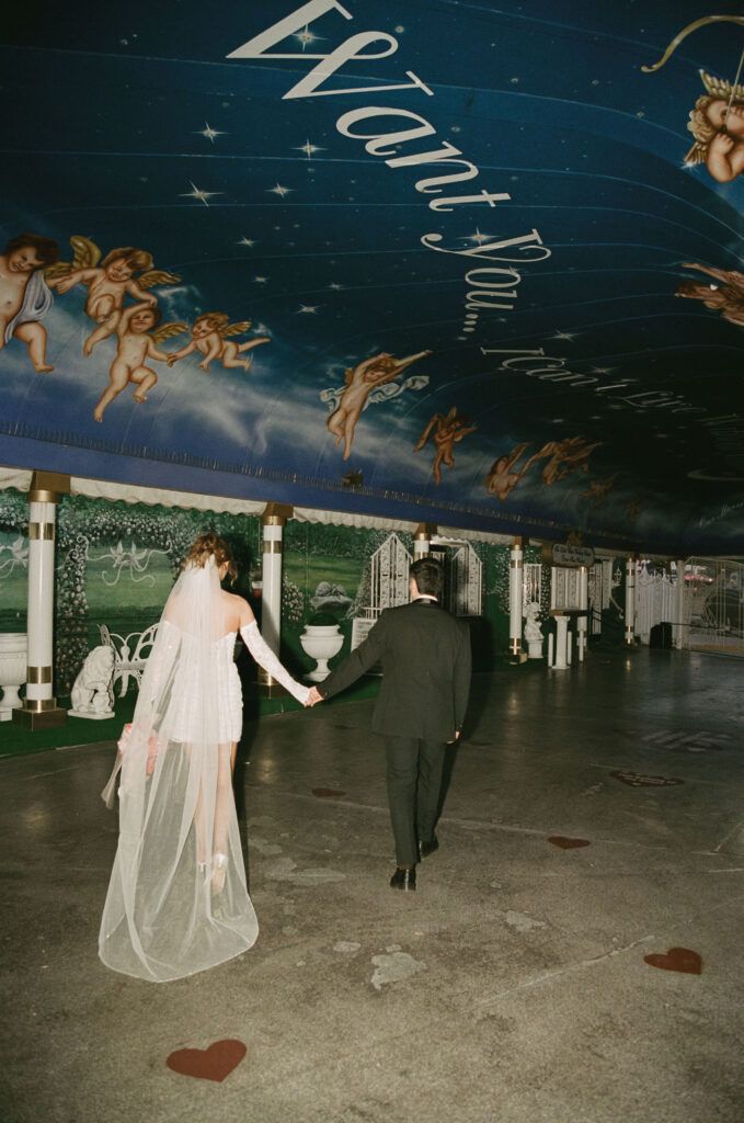 Bride and groom holding hands walking away under the painted tunnel at The Little White Wedding Chapel.