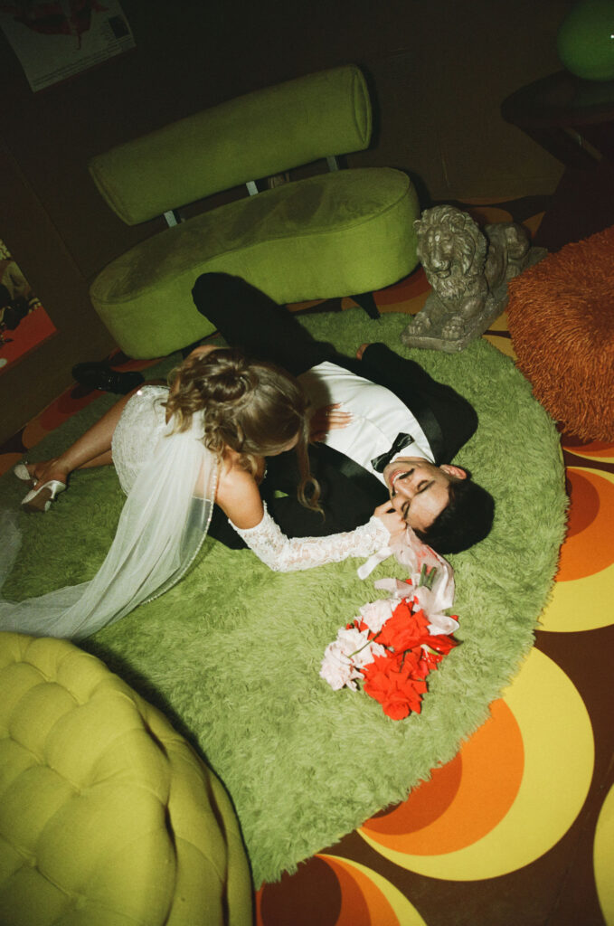 Bride and groom laying on a green shag rug, laughing together inside a vintage Las Vegas mini-mansion.