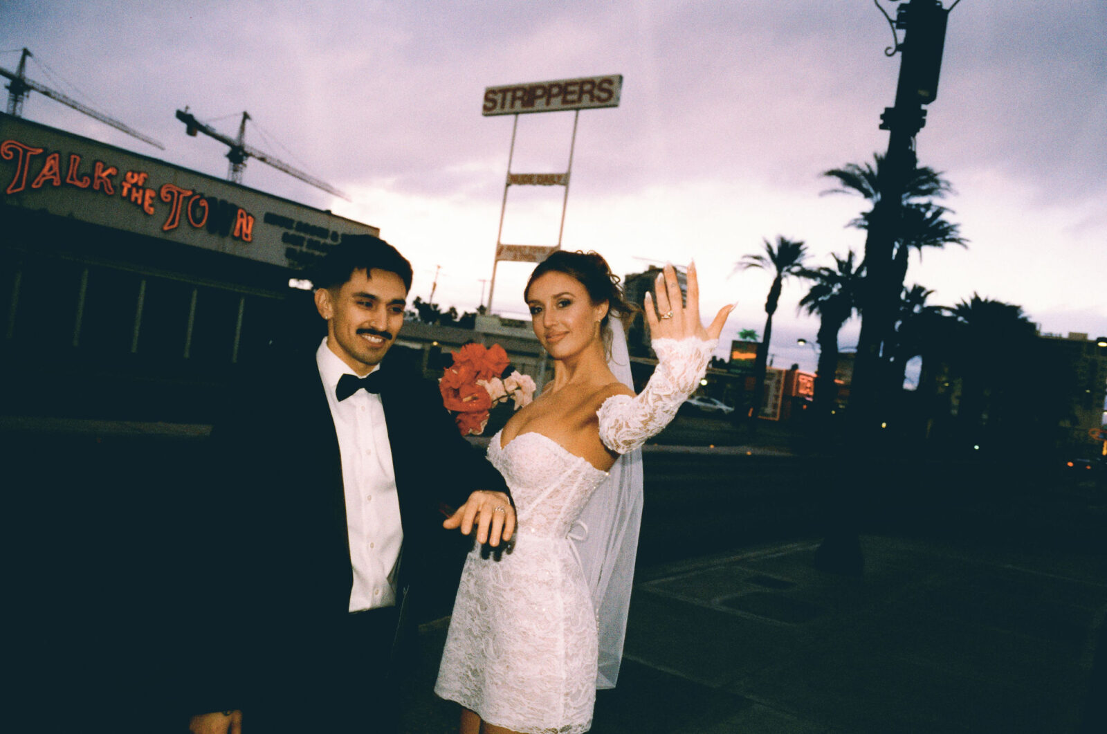 Bride and groom showing off their rings outside a neon Vegas strip club sign, photographed on film.