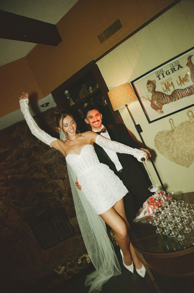 Bride pouring champagne into a stacked champagne tower during a retro film elopement reception.