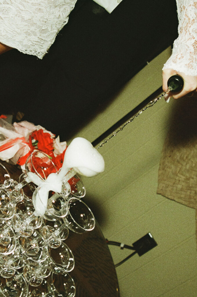 Bride pouring champagne into a stacked champagne tower during a retro film elopement reception.