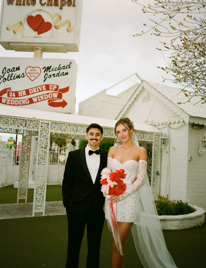 Bride and groom posing outside of The Little White Wedding Chapel on film