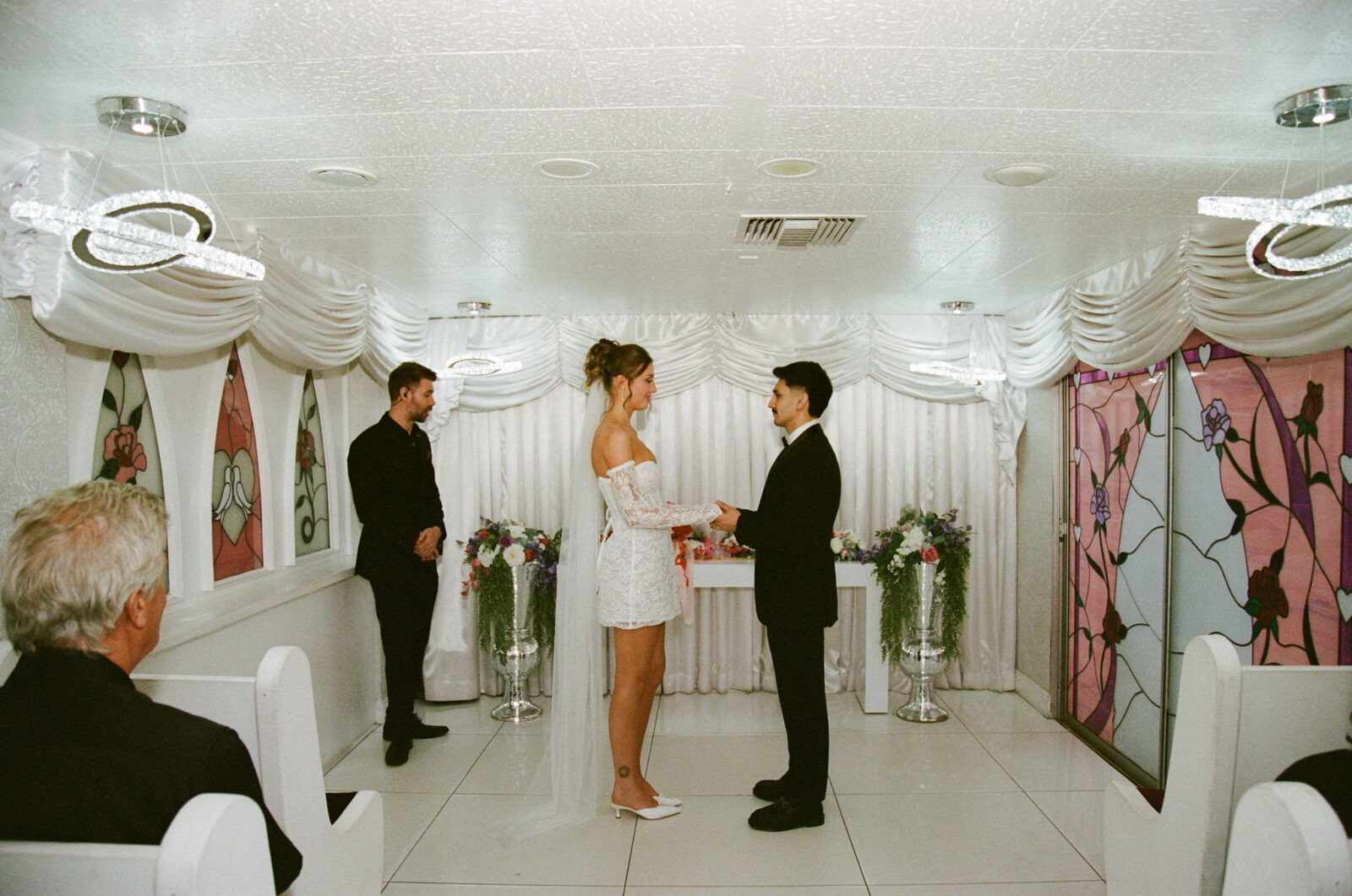 Bride and groom holding hands at the altar during their Little White Wedding Chapel ceremony on film