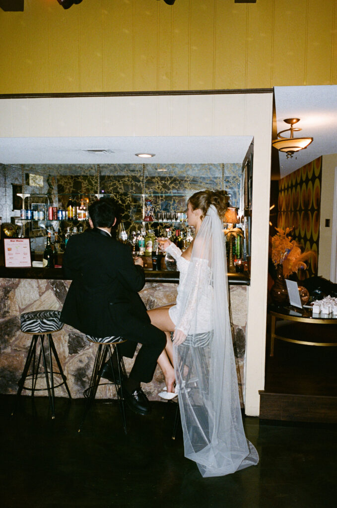 Bride and groom sitting at the built-in bar of a vintage Las Vegas home, enjoying drinks together.