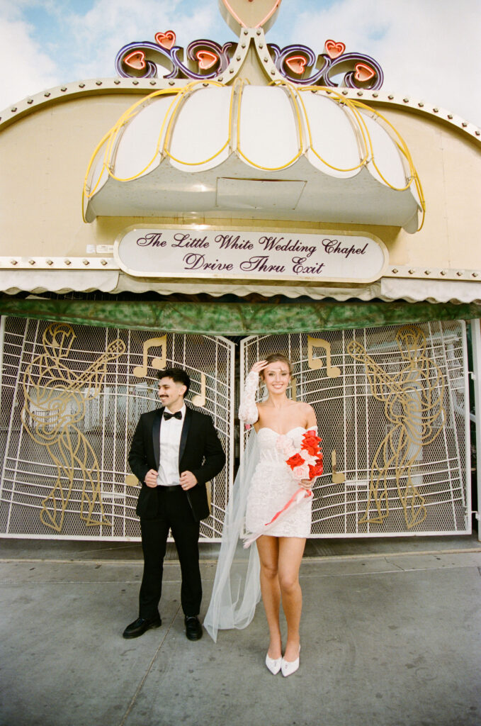 Bride and groom smiling outside The Little White Wedding Chapel under the vintage drive-thru wedding sign.
