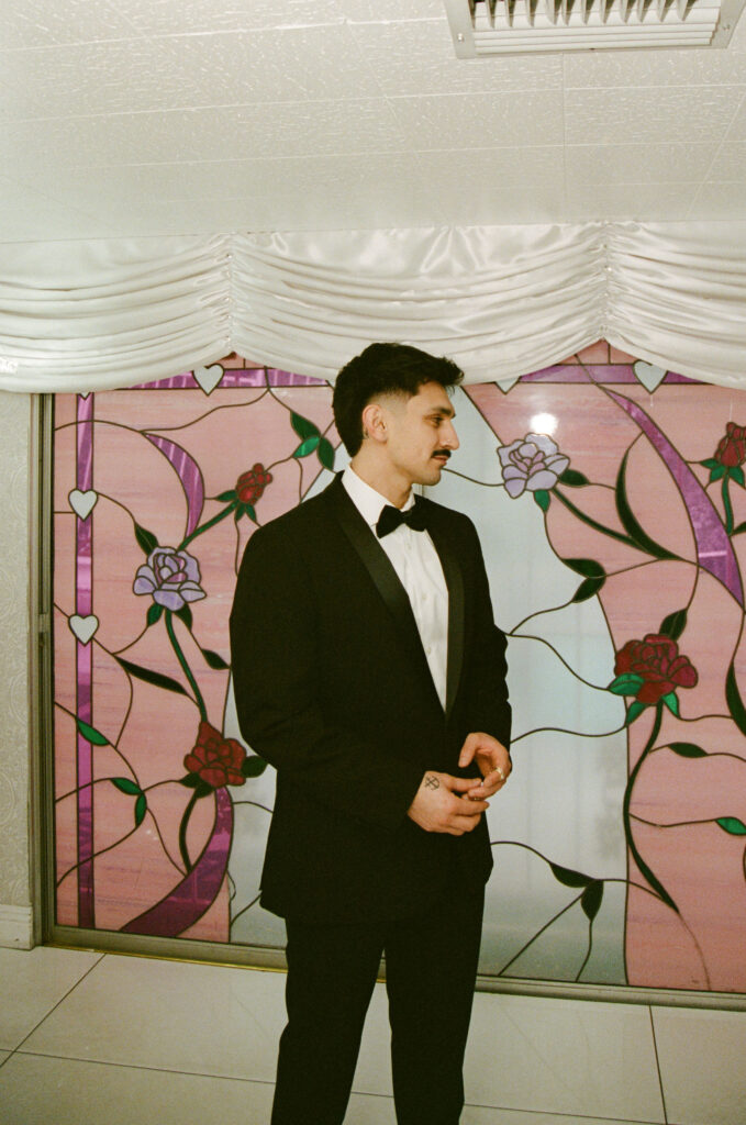 Groom standing in front of stained glass window inside The Little White Wedding Chapel on film