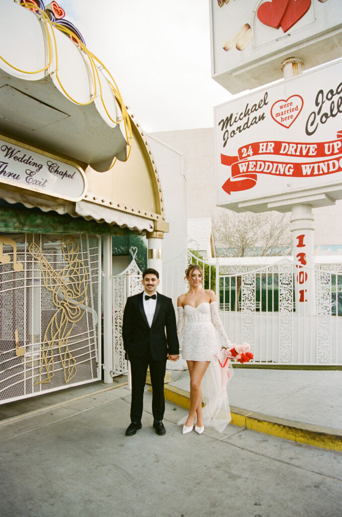 Bride and groom posing outside of The Little White Wedding Chapel on film