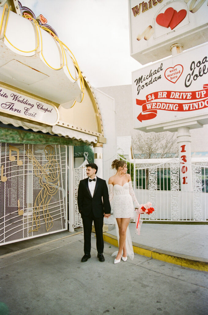 Bride and groom posing outside the Little White Wedding Chapel drive-thru exit sign.