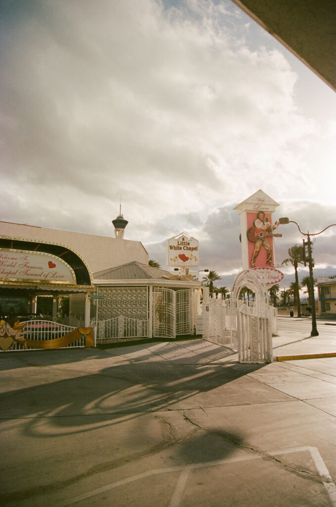 Exterior shot of The Little White Wedding Chapel with cloudy skies and the Stratosphere tower in the background on film