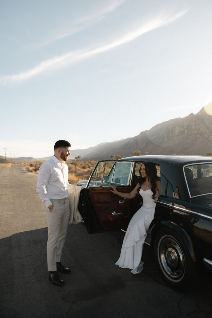 Woman stepping out of a vintage car while her partner looks on during Las Vegas desert engagement photos.
