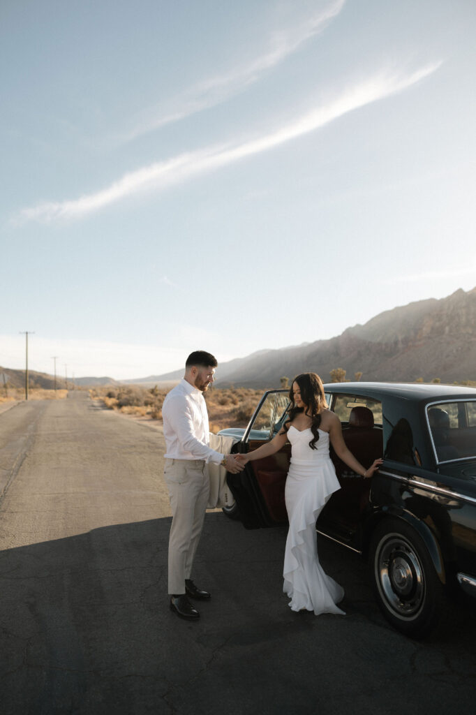 Woman stepping out of a vintage car while her partner looks on during Las Vegas desert engagement photos.
