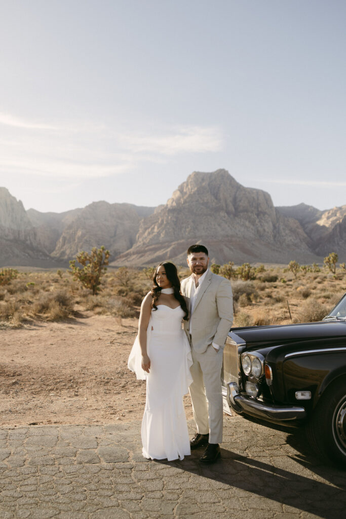 Couple posing beside a classic black Rolls-Royce at Red Rock Canyon during their desert engagement photos.
