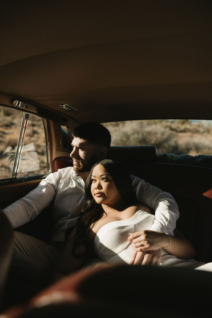 Couple sitting in the backseat of a classic Rolls-Royce with sunlight streaming through the window at Red Rock Canyon.