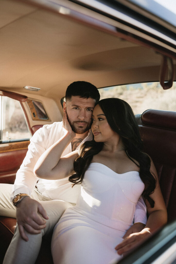 Couple sitting close together inside a classic car, soft desert light pouring through the window during Red Rock Canyon engagement photos.