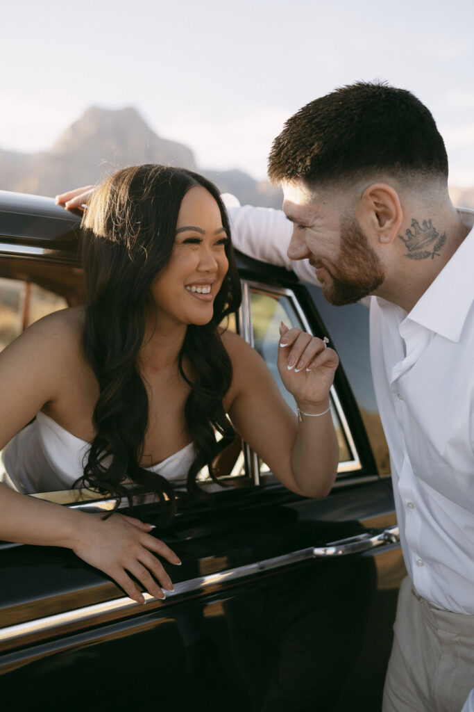Couple smiling and leaning toward each other through a car window during desert engagement photos in Las Vegas.
