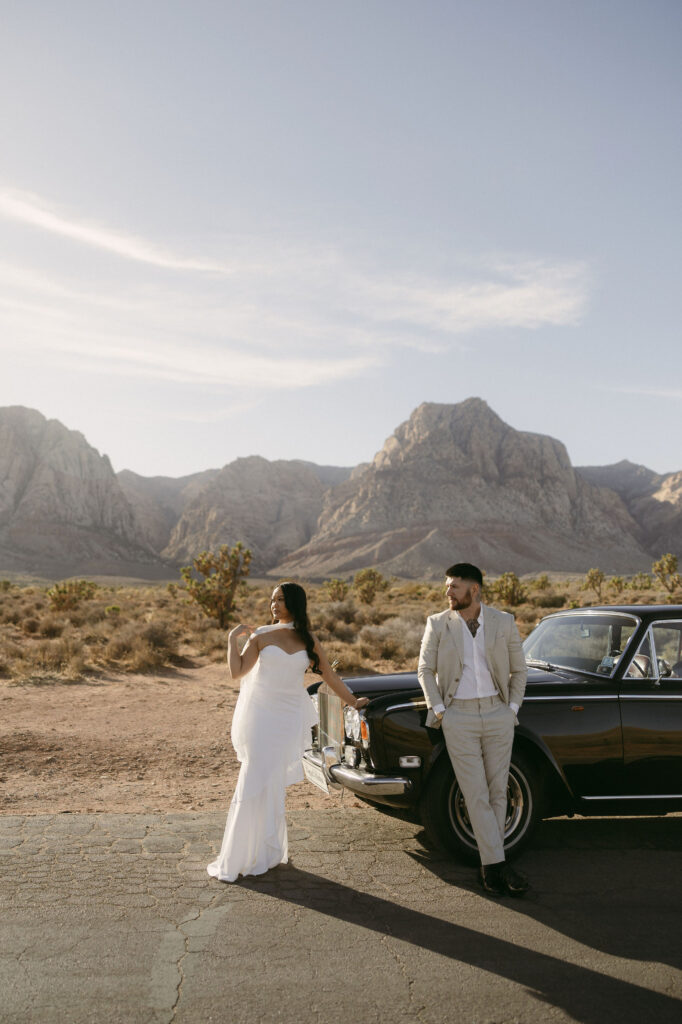 Couple posing beside a classic black Rolls-Royce at Red Rock Canyon during their desert engagement photos.
