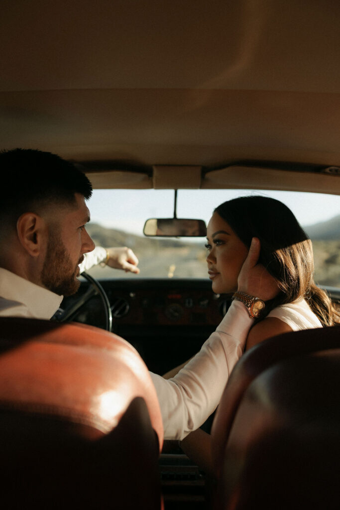 Couple sitting in the front seat of a vintage car with desert sunlight streaming through the window during Red Rock Canyon engagement photos.