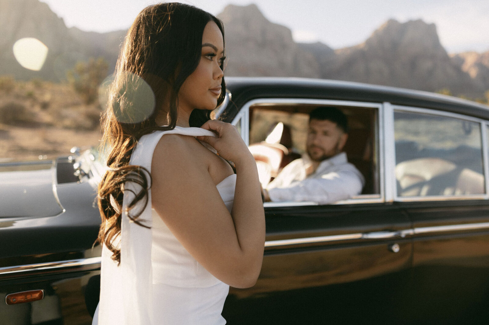 Close-up of a woman adjusting her dress while standing beside a classic car during desert engagement photos in Las Vegas.