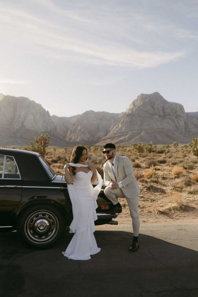 Couple posing beside a classic black Rolls-Royce at Red Rock Canyon during their desert engagement photos.