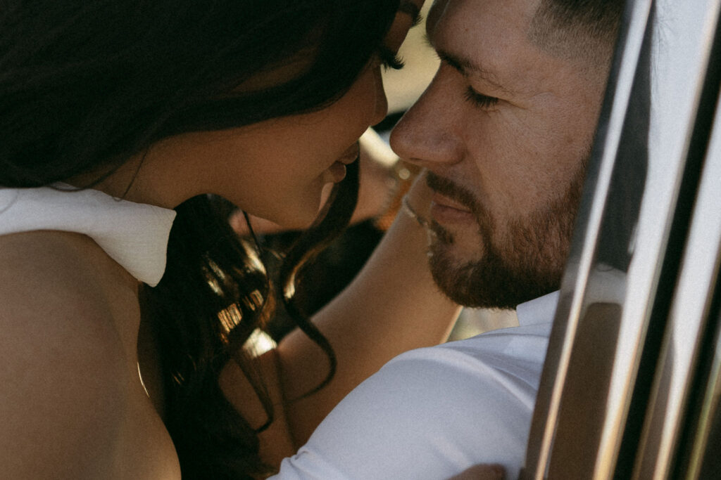 Intimate close-up of a couple leaning in for a kiss beside a classic car during desert engagement photos.