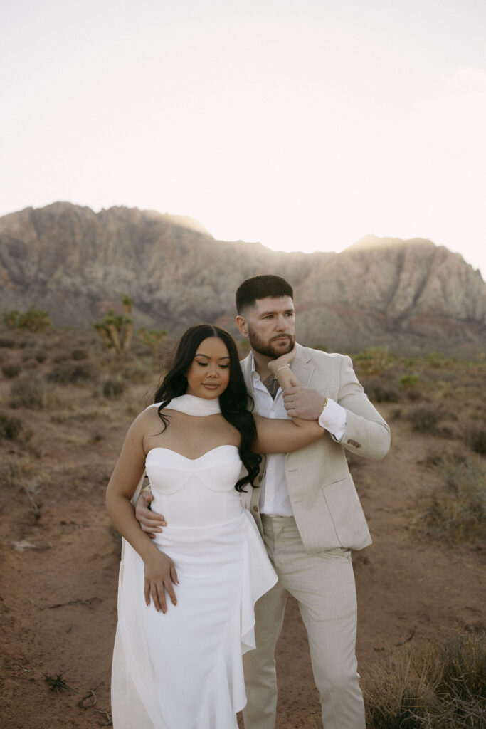 Groom adjusts his partner’s arm while posing in the desert with mountain views at Red Rock Canyon.