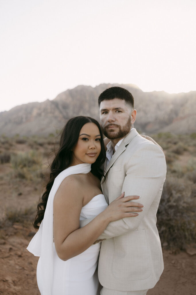 Couple embracing closely at sunset with the desert mountains behind them at Red Rock Canyon.