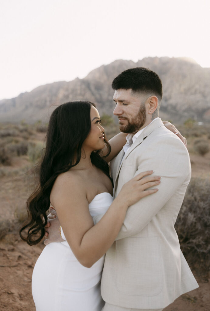 Couple embracing closely at sunset with the desert mountains behind them at Red Rock Canyon.