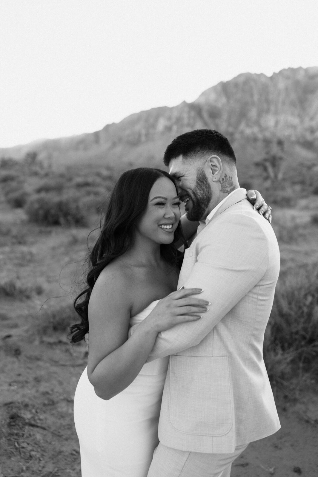 Black-and-white photo of the couple laughing and holding each other during their Las Vegas desert engagement session.