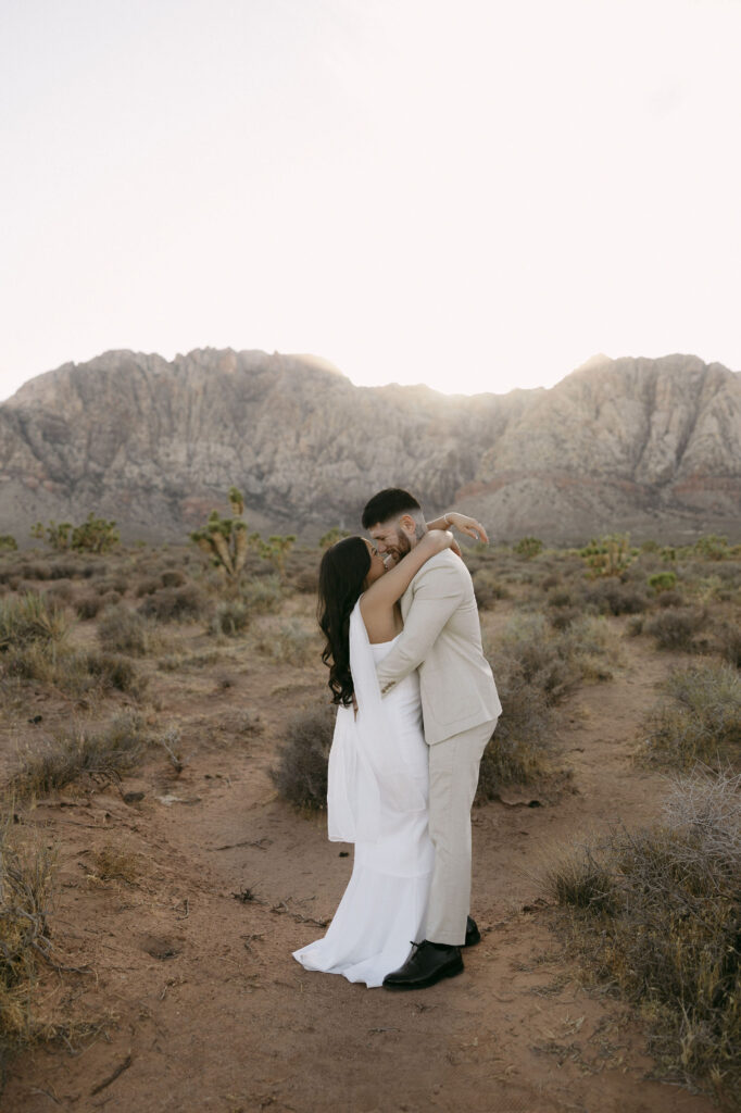 Couple sharing a kiss surrounded by desert brush and mountains at Red Rock Canyon.