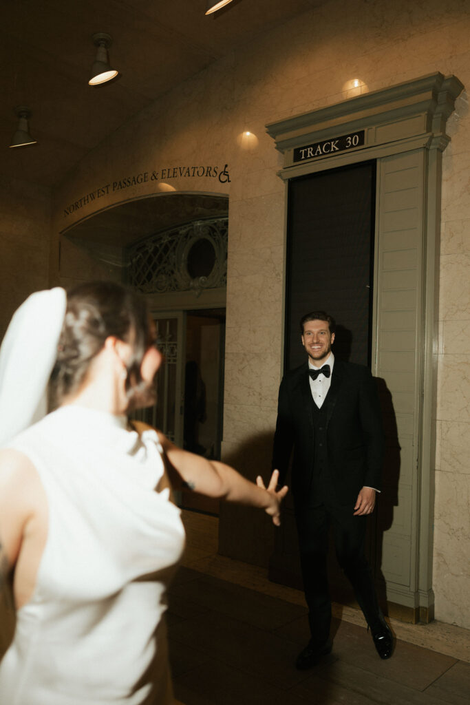 Bride reaching toward her partner inside Grand Central Station during candid wedding portraits.