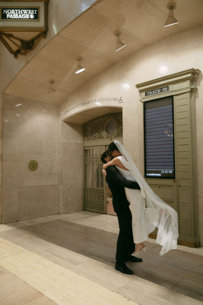 Couple embracing beneath signage inside Grand Central Station after their New York City Hall elopement.