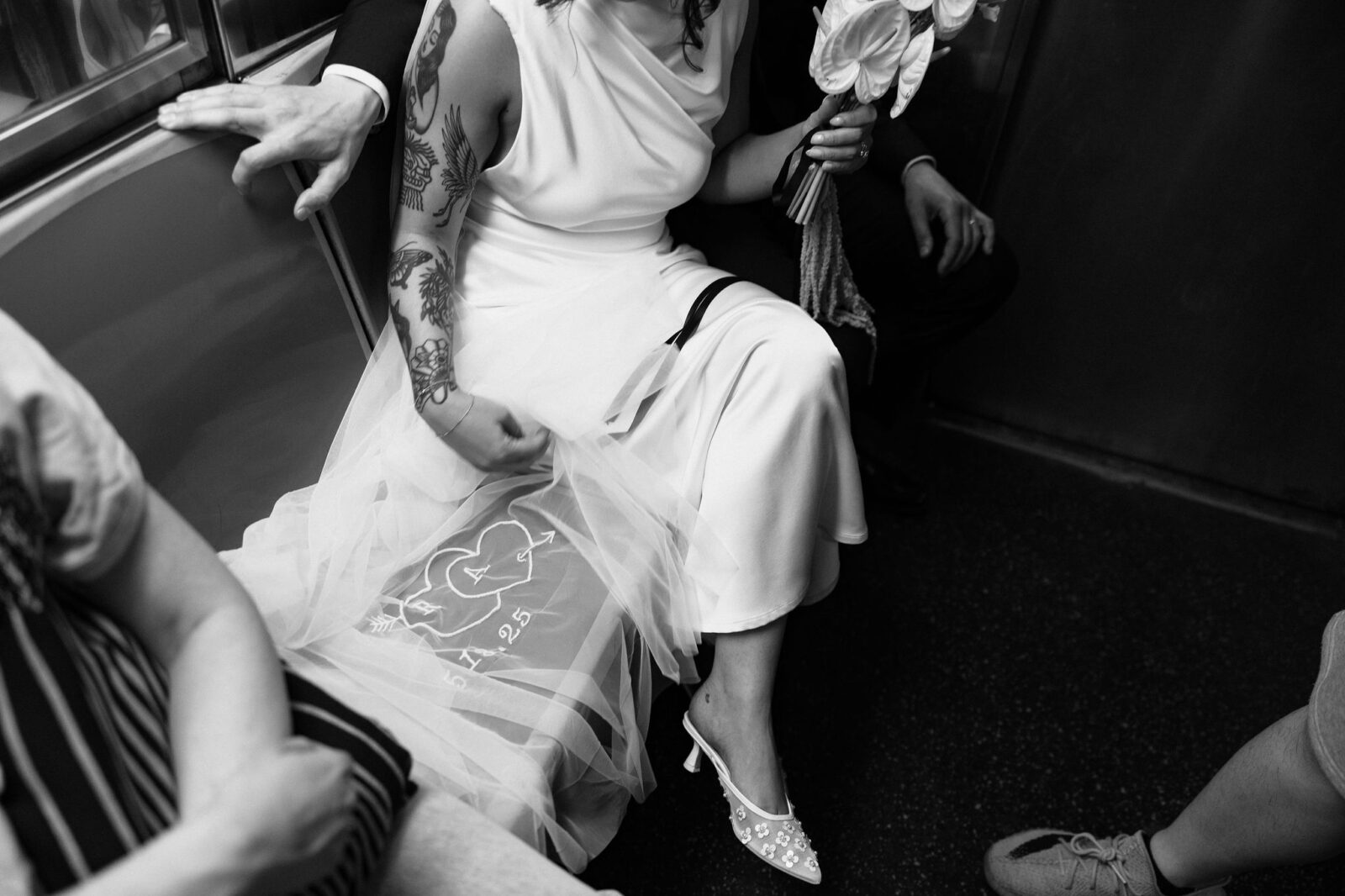 Black and white photo of a bride’s dress and heels on the subway after a New York City Hall elopement.