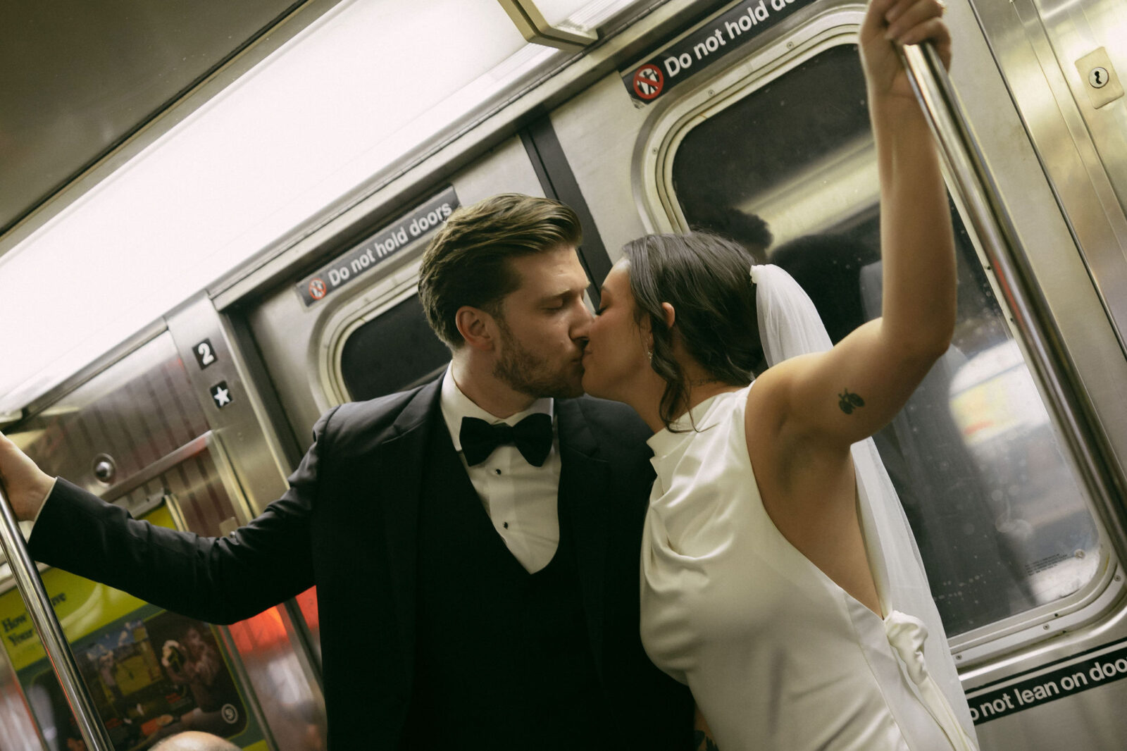 Bride and groom kissing on a subway train. 