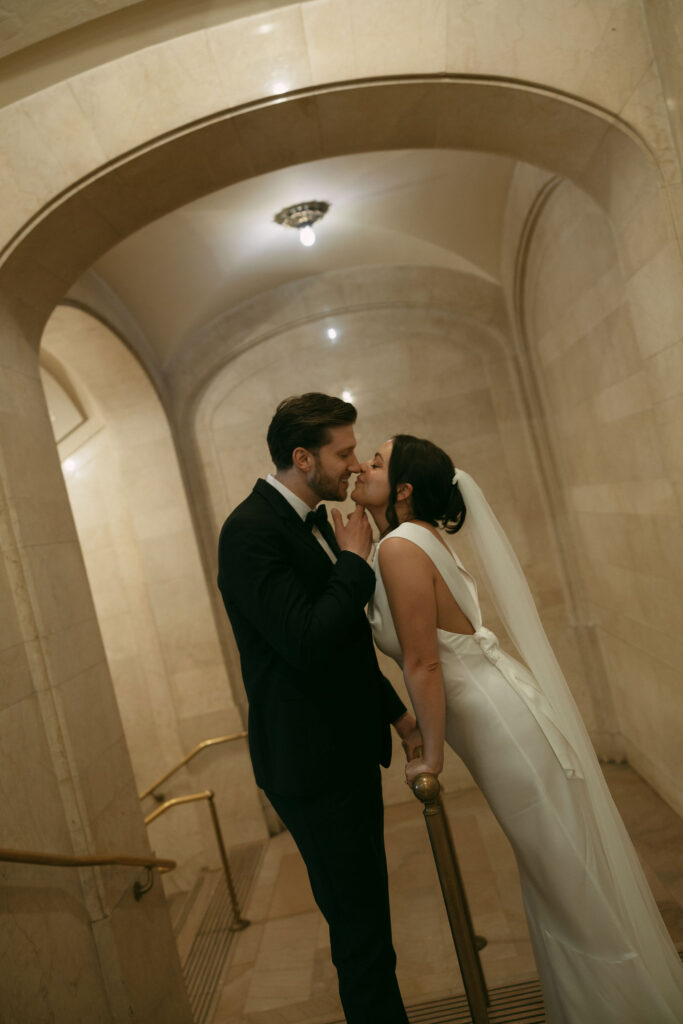 Couple sharing a quiet kiss on a marble staircase inside Grand Central Station after their elopement.