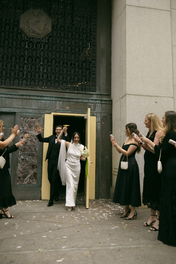 Couple exiting Manhattan City Hall during a New York City Hall elopement as friends toss confetti.