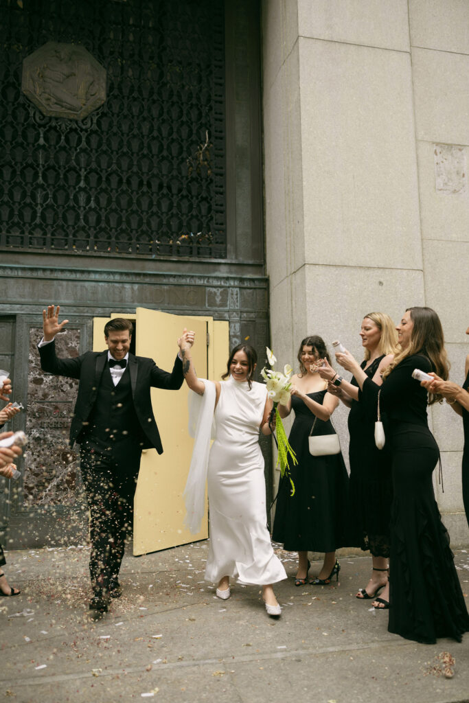Bride and groom celebrating outside Manhattan City Hall during their New York City Hall elopement with friends tossing confetti.