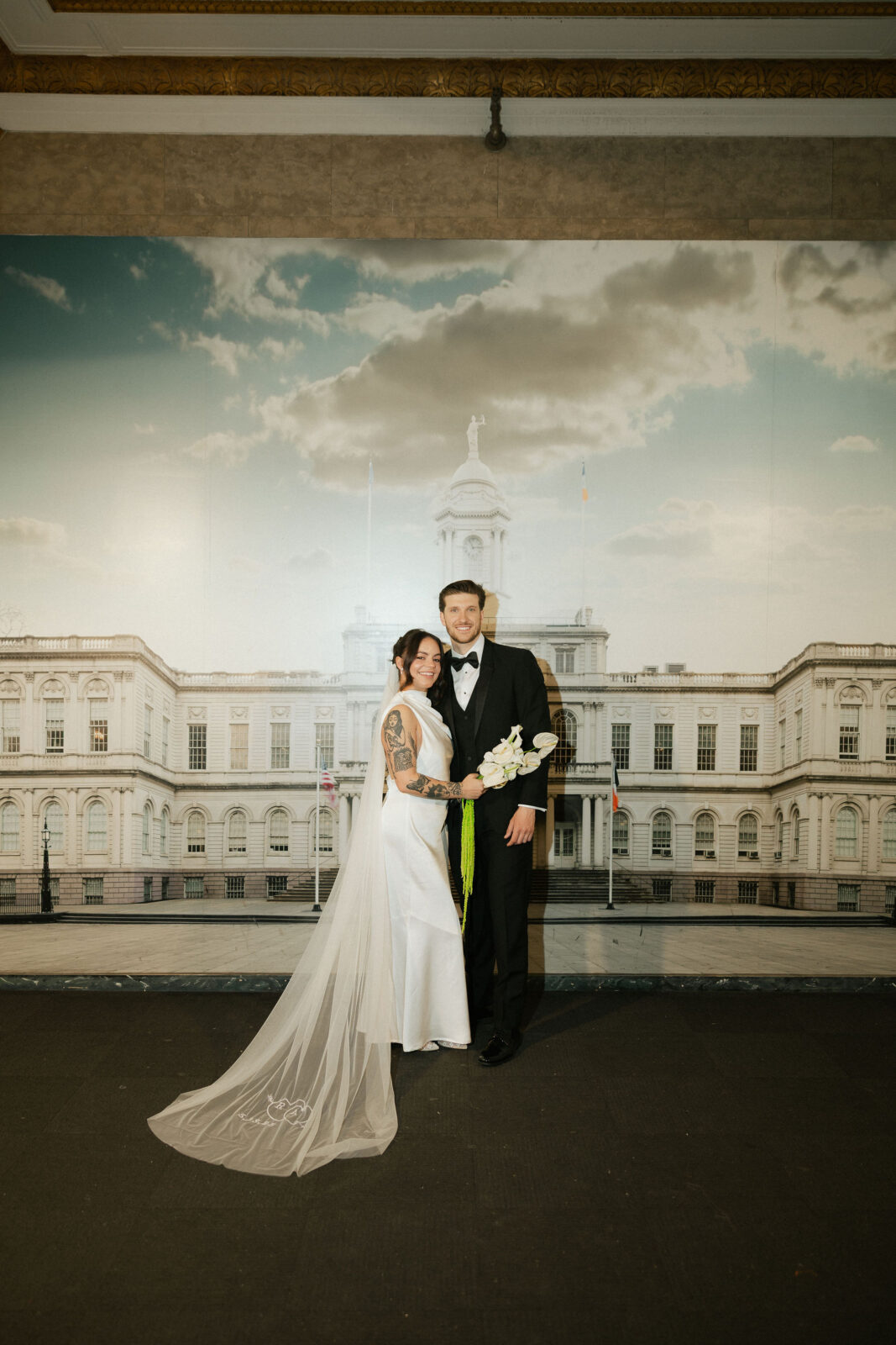 Bride and groom posing together inside Manhattan City Hall during a New York City Hall elopement, holding a white lily bouquet.
