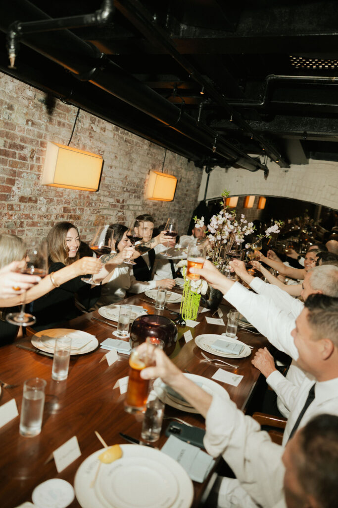Friends and family raising glasses in a toast during an intimate Sartiano’s dinner after a New York City Hall elopement.